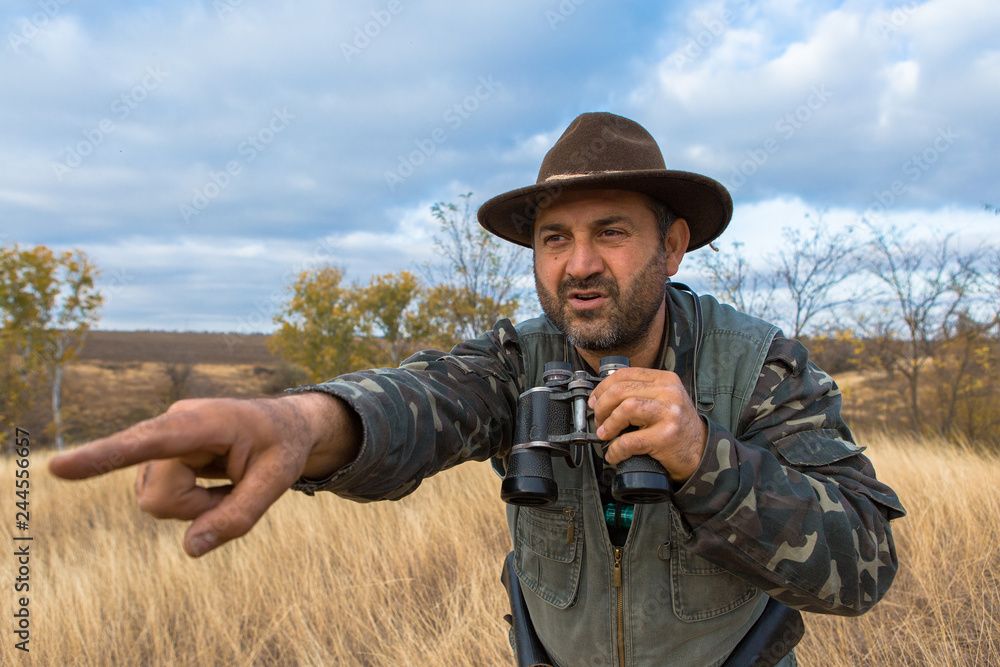 A hunter in a hat with binoculars looks out for prey A hunter in a hat with binoculars looks out for prey