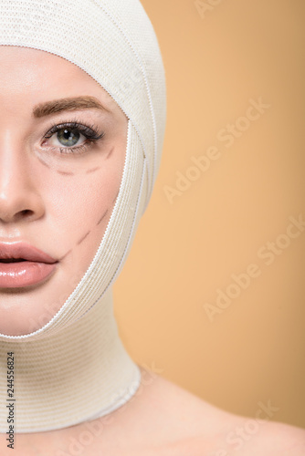 cropped shot of woman with bandages over head and correcting marks on face looking at camera isolated on beige
