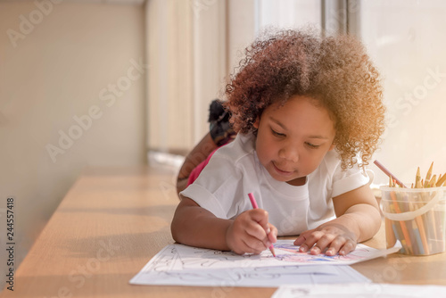 Little toddler girl laying down concentrate on drawing.  Mix African girl learn and play in the pre-school class. Children enjoy hand writing. 3 years girl enjoy playing at nursery. photo
