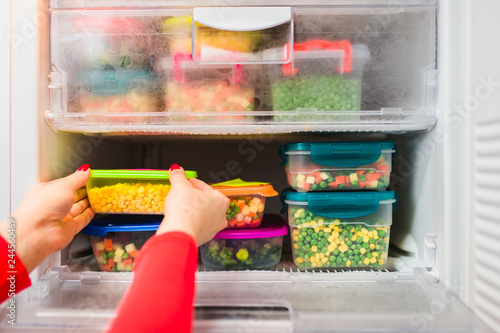 Woman placing container with frozen mixed vegetables in refrigerator. photo