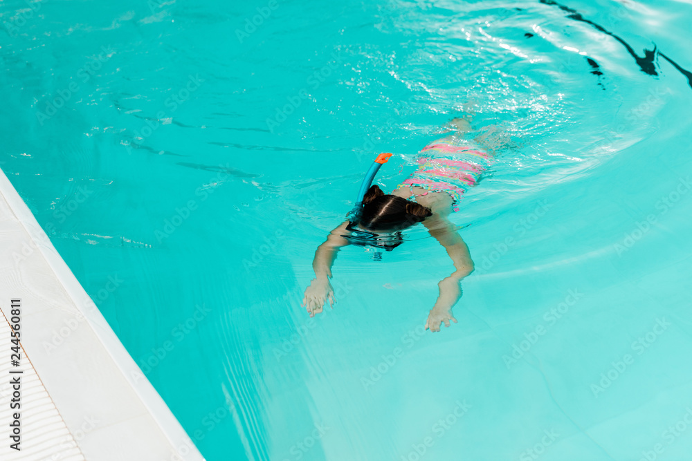 child snorkeling in blue water in swimming pool