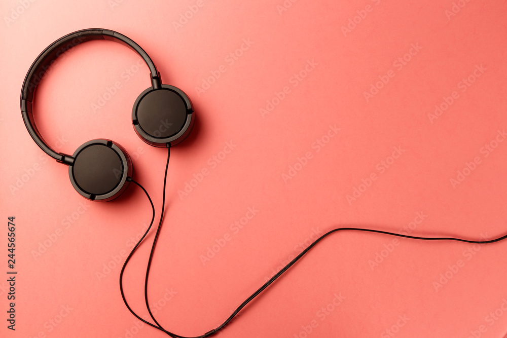 Headphones on coral background. Black headphones on a pastel background. Top view. Flat lay. Copy space. Living Coral color of the Year 2019. Minimal style with colorful paper backdrop. Music concept Headphones on coral background. Black headphones on a pastel background. Top view. Flat lay. Copy space. Living Coral color of the Year 2019. Minimal style with colorful paper backdrop. Music concept