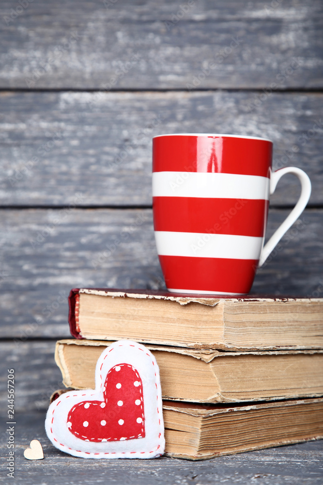 Obraz premium Fabric heart with cup and old books on wooden table