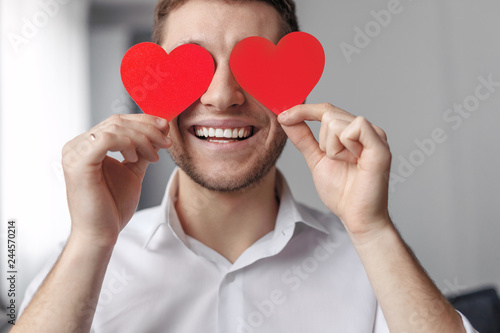 Cheerful guy holding hearts near face