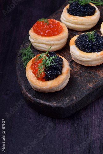Red and black caviar in tartlets on a wooden board