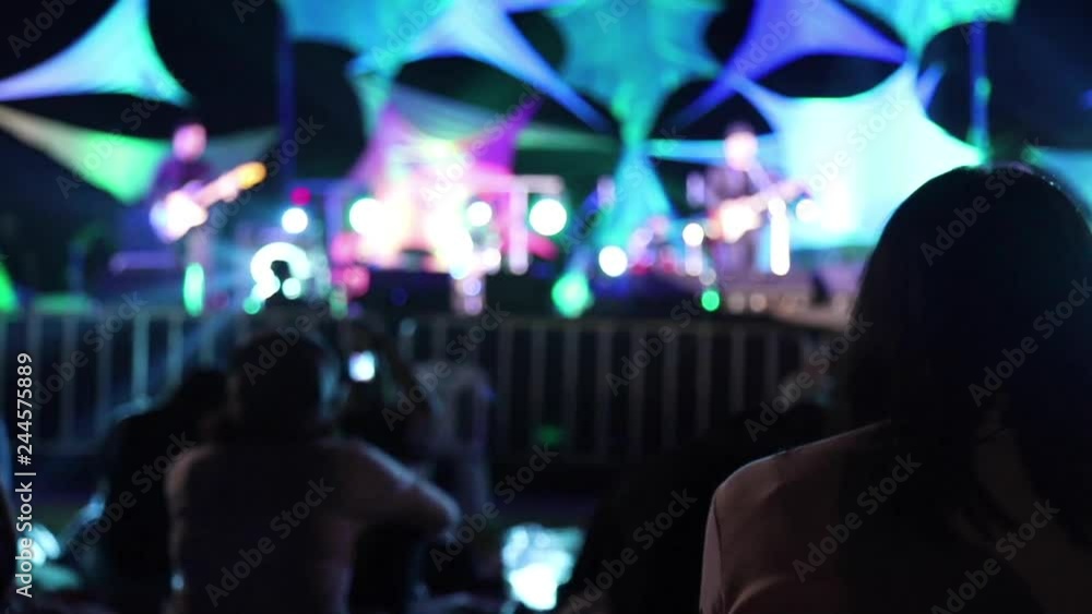 People are sitting in front of the music concert with lighting on the stage. People are sitting in front of the music concert with lighting on the stage.