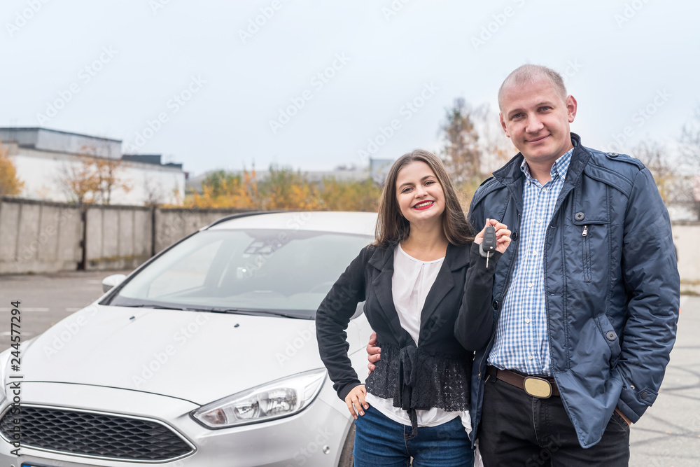 Smiling couple posing near new car with keys Smiling couple posing near new car with keys