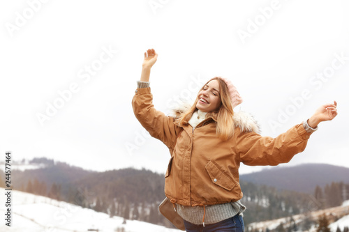 Young woman in warm clothes near snowy hill, space for text. Winter vacation