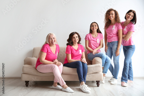 Group of women with silk ribbons on sofa near light wall. Breast cancer awareness concept