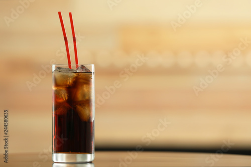 Glass of cola with ice on table against blurred background. Space for text