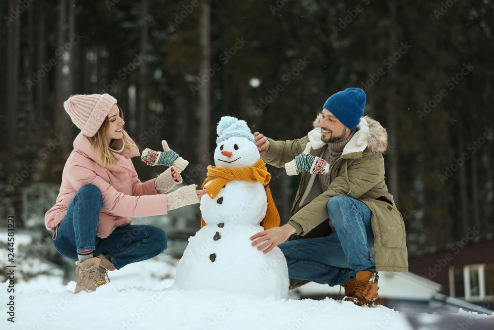 Fototapeta premium Couple making snowman outdoors. Winter vacation