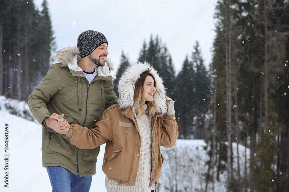 Fototapeta premium Happy couple near conifer forest on snowy day, space for text. Winter vacation