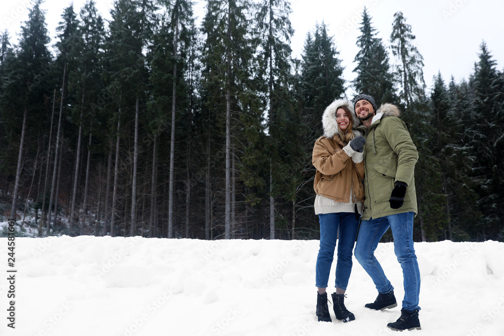 Couple near conifer forest on snowy day, space for text. Winter vacation