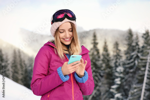 Young woman with ski goggles using smartphone in mountains during winter vacation