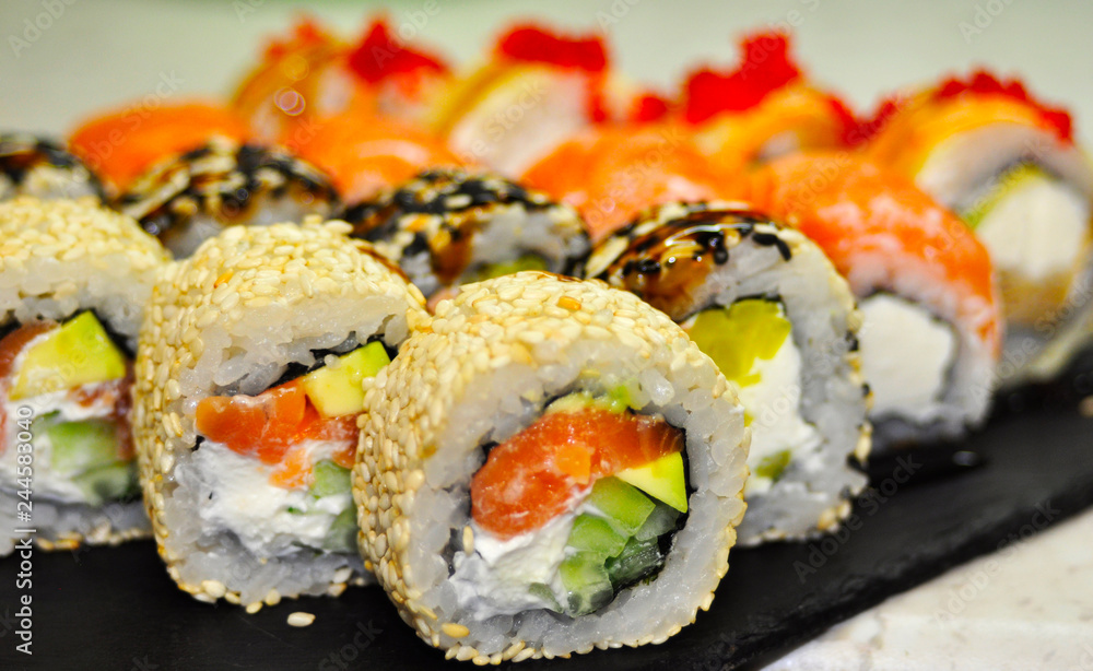 Eating Sushi with chopsticks. Sushi roll japanese food in restaurant. California Sushi roll set with salmon, vegetables, flying fish roe and caviar closeup. Japan restaurant menu Eating Sushi with chopsticks. Sushi roll japanese food in restaurant. California Sushi roll set with salmon, vegetables, flying fish roe and caviar closeup. Japan restaurant menu