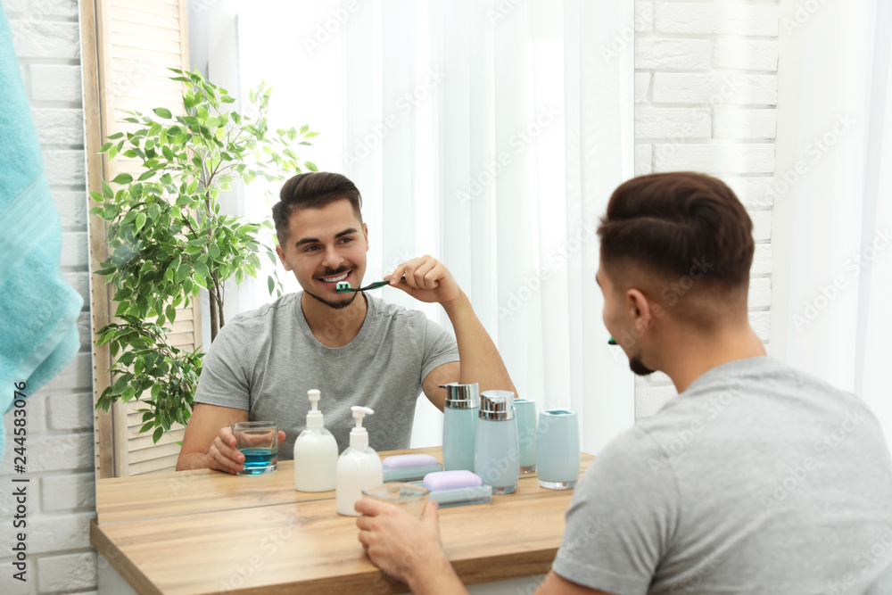 Young man brushing teeth near mirror in bathroom at home