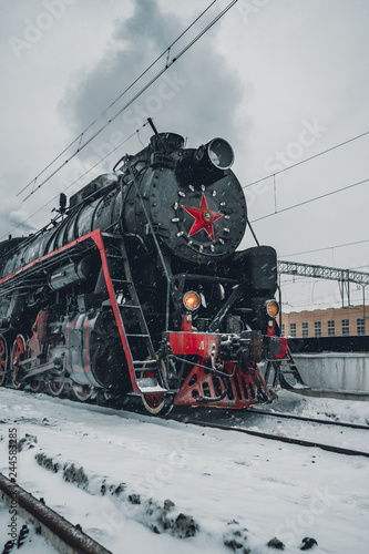 Vintage Black and Red Steam Locomotive Train in Winter. Clouds of smoke and clean white sky, snow all around