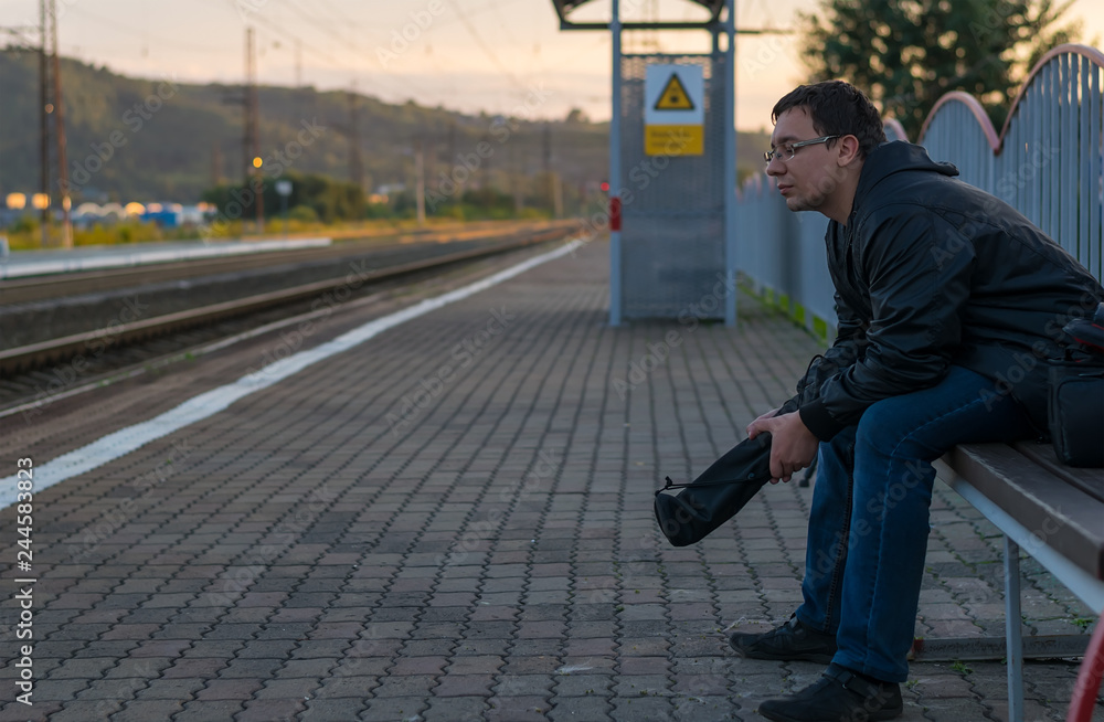 Man sitting on the street on the platform on a bench with a sad face, thinking and waiting for the train