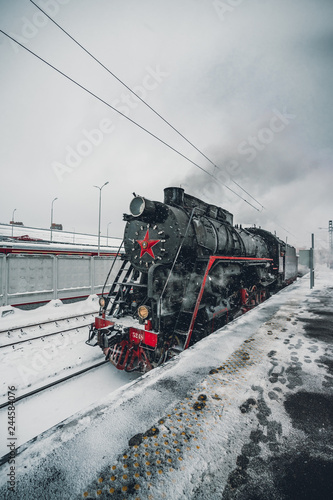 Vintage Black and Red Steam Locomotive Train in Winter. Clouds of smoke and clean white sky, snow all around