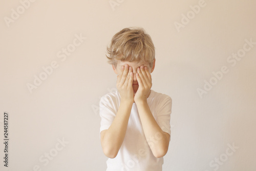Eyes closed palms. I see nothing. The boy closed his eyes with his palms. Light background.