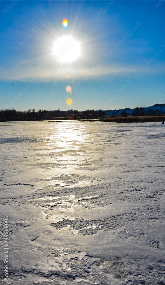 Fototapeta premium snowy winter day outdoor. ice-bound lake with blue sky and bright sun over it.