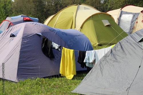 Wet clothes dried on a rope stretched between the tents - tourist life, camp tents on the green grass on the trees background on summer day - sports tourism, camping, scouting