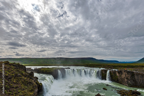 Godafoss waterfall landscape covered with clouds crossed by sunlight.