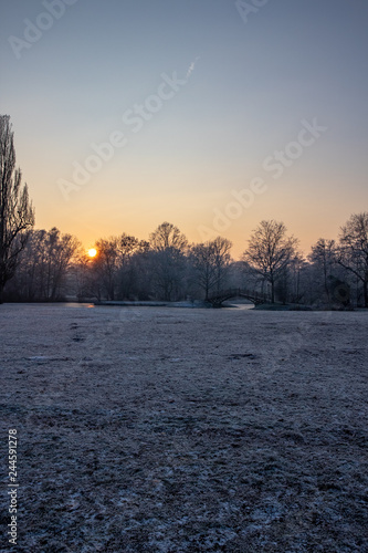 Zugefrorener Teich im Park mit Romantischen Brücken im Winter in Leipzig bei frostigen Wetter mit Sonnenuntergang