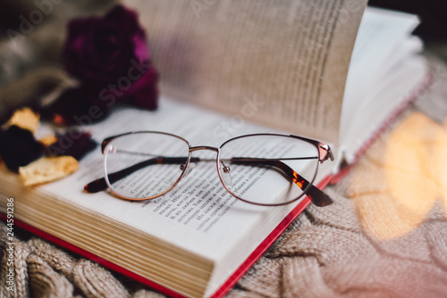 Glasses are on the open book. Cozy atmosphere. Soft focus.