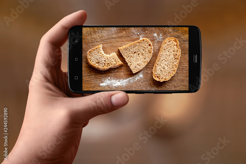 Men hands  takes photography of food on table with phone. Slices of bread and flour on a wooden board. Smartphone photo for post on social networks. photo