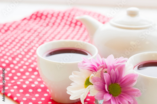 Black tea ceremony - a cup of tea, teapot, flowers on a red with white dots background