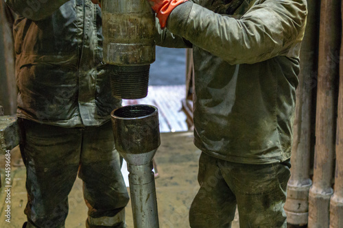 Offshore oil rig worker prepare tool and equipment for perforation oil and gas well at wellhead platform. Making up a drill pipe connection. A view for drill pipe connection from between the stands. photo