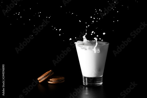 Spalsh in glass of milk and chocolate cookies on black background