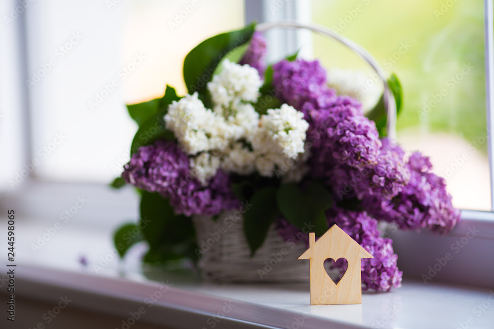 Wooden house with hole in form of heart and tender bouquet of beautiful lilac in white basket near window in daylight. Wooden house with hole in form of heart and tender bouquet of beautiful lilac in white basket near window in daylight.
