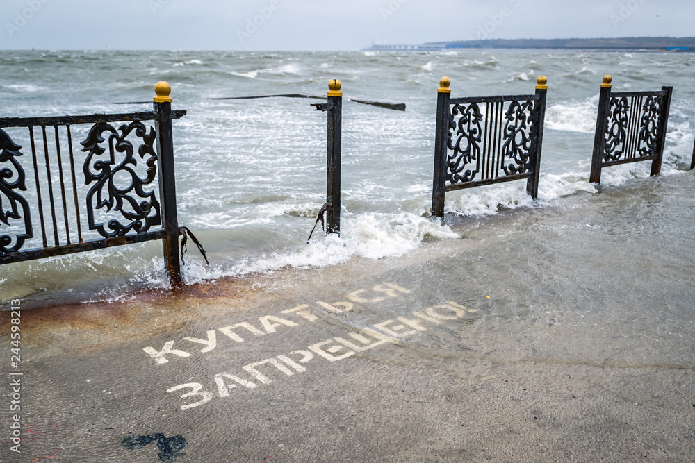 Broken metal fence on the sea embankment during a strong storm and the inscription on the pier - swimming is prohibited, no swimming
