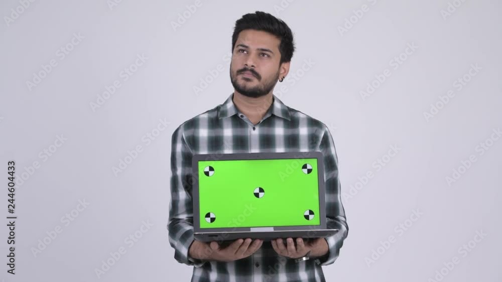 Portrait of young happy bearded Indian man thinking while showing laptop Portrait of young happy bearded Indian man thinking while showing laptop
