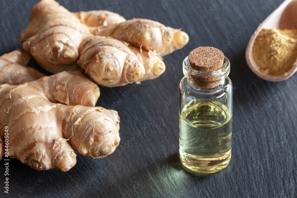 A bottle of ginger essential oil with fresh and ground ginger