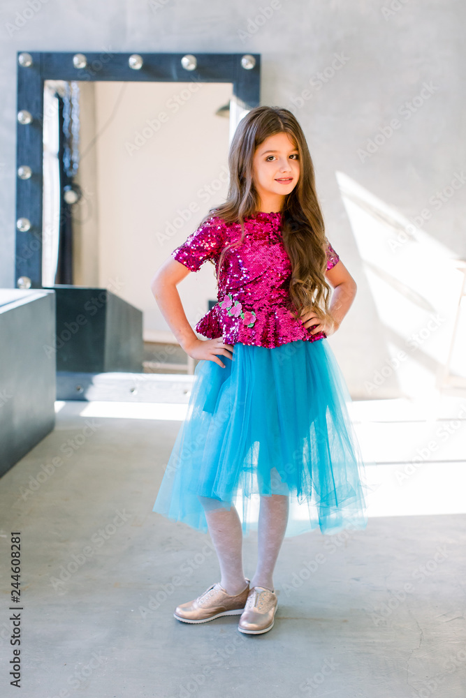 Portrait of little fashion kid girl in a pink shiny blouse and a blue skirt on gray loft background Stock Photo Adobe Stock