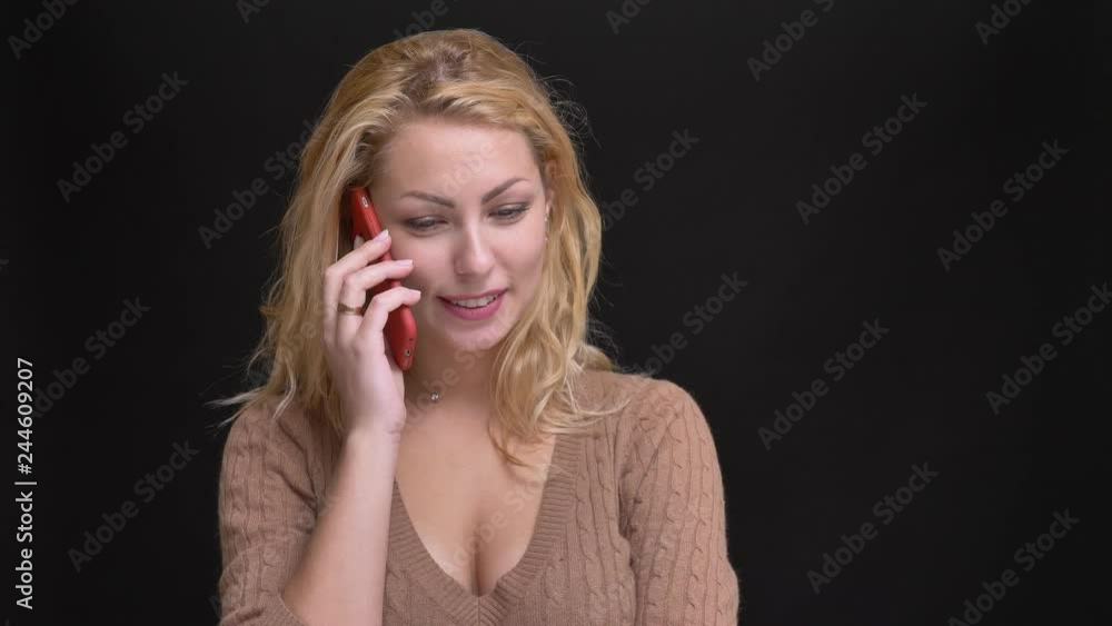 Portrait of beautiful caucasian long-haired woman smilingly talking on smartphone on black background. Portrait of beautiful caucasian long-haired woman smilingly talking on smartphone on black background.