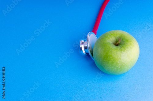 Green Apple with medical stethoscope isolated on blue background for healthy eating. Selective focus and crop fragment. Healthy, Diet and copy space concept photo