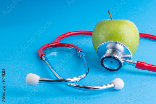 Green Apple with medical stethoscope isolated on blue background for healthy eating. Selective focus and crop fragment. Healthy, Diet and copy space concept photo