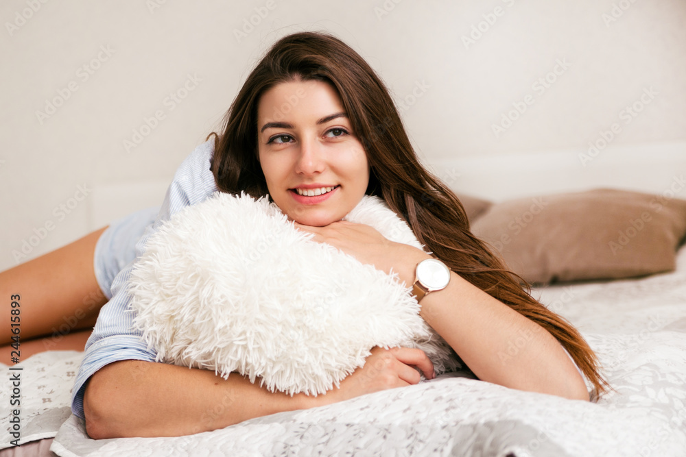 Young smiling woman lying with pillow in bed in her bedroom. Happy morning. Young smiling woman lying with pillow in bed in her bedroom. Happy morning.