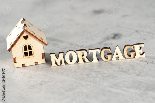 Model wooden house with wooden letters next to which make up the word mortgage on the litter concrete background. Mortgage concept. Selective focus