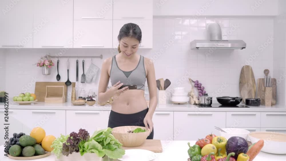 Young Asian blogger woman using smartphone photo post in social media in the kitchen, female in sport clothing making salad at home. Lifestyle women relax at home concept. Young Asian blogger woman using smartphone photo post in social media in the kitchen, female in sport clothing making salad at home. Lifestyle women relax at home concept.