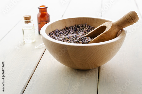 Fototapeta Naklejka Na Ścianę i Meble -  Herbal Lavender Buds in Wooden Bowl with Glass Bottles containing Oils on Wood Plank Table
