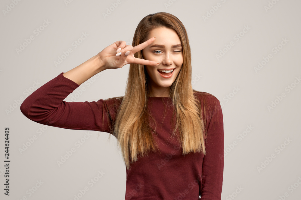 Portrait of young female showing two fingers and winking at the camera. Copy space wall for your information or advertising content Portrait of young female showing two fingers and winking at the camera. Copy space wall for your information or advertising content
