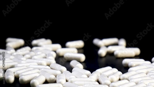 White pills drugs vitamin or minerals are poured out of jar on black table