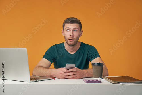 фотографія Portrait of bored good-looking man, holding cell phone, looking up having pensive expression