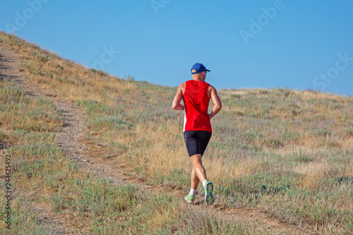 rear view of athletic runner running on a mountain trail on a blue sky background