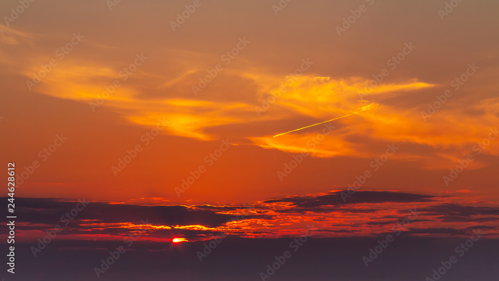 sky during a colorful, bright orange sunset, sun's rays make their way through the clouds